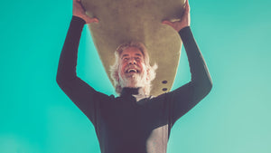 older man holding surfboard smiling