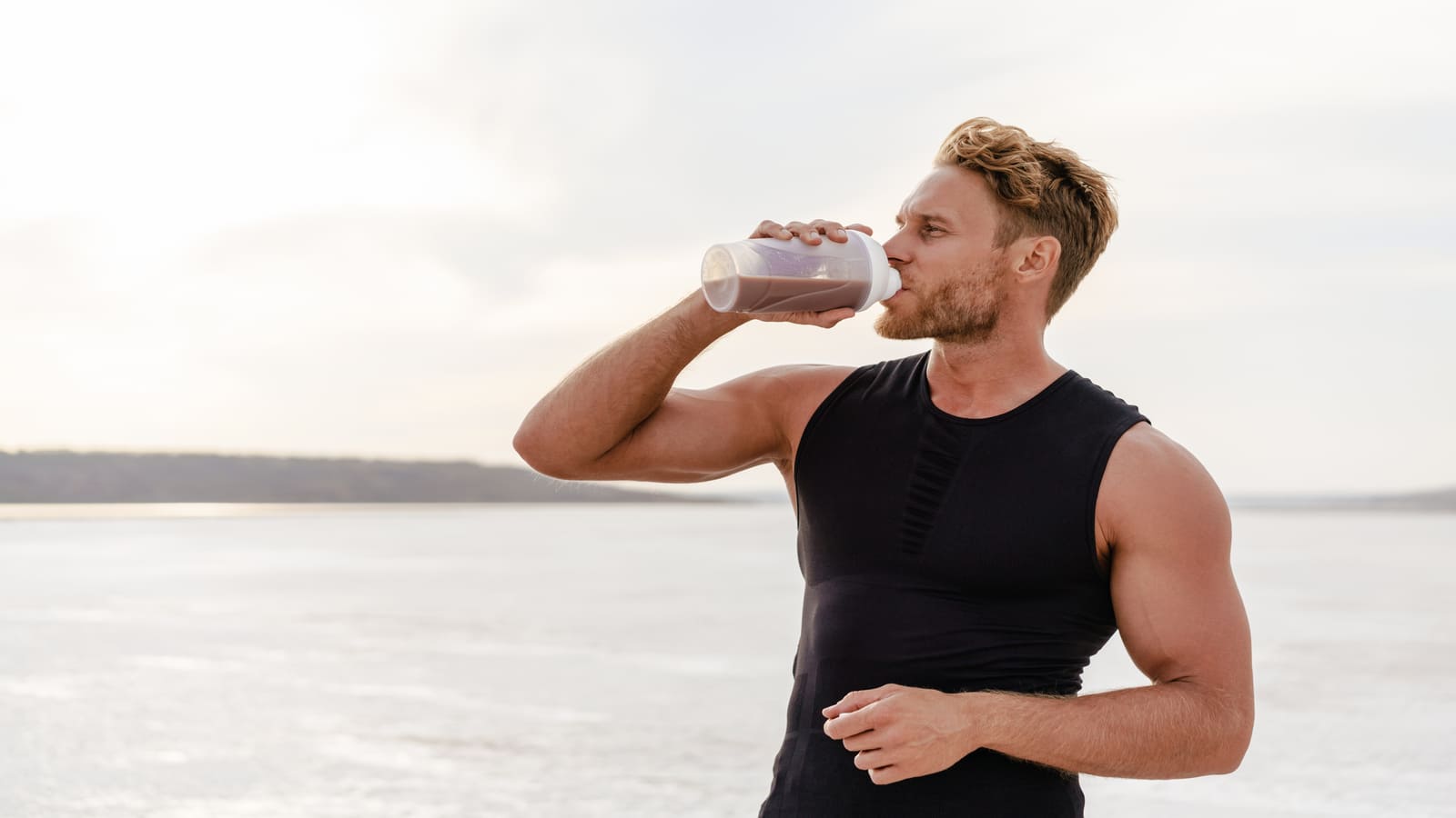 man drinking protein shake on beach