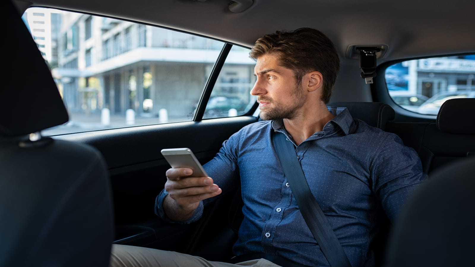 stressed man looking out car window holding phone